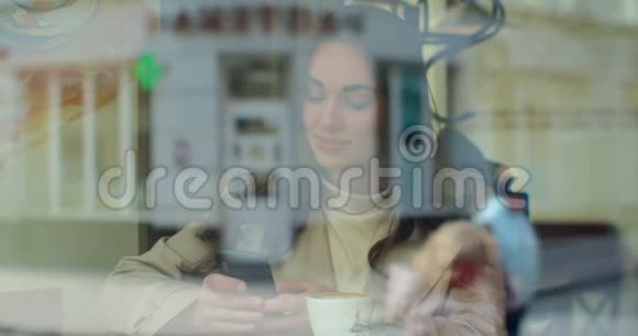 使用智能手机在咖啡馆喝咖啡的年轻女性在社交媒体上发短信享受移动技术视频的预览图