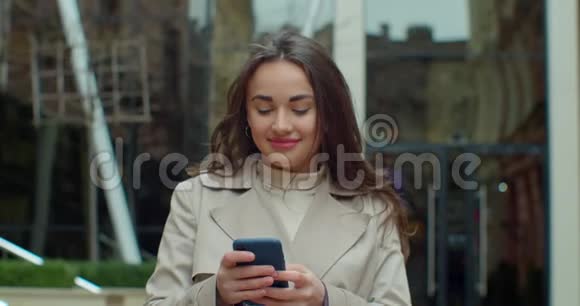 漂亮的年轻女人在现代化的大办公楼附近用电话走路和朋友聊天女孩用手机视频的预览图