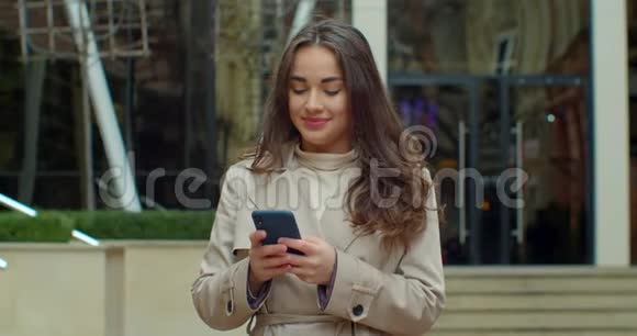 有魅力的年轻女性在大现代办公楼附近使用电话行走和朋友聊天女孩用手机视频的预览图
