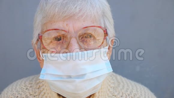 戴眼镜的奶奶戴防病毒面具的肖像奶奶用沉思的目光看着镜头概念视频的预览图