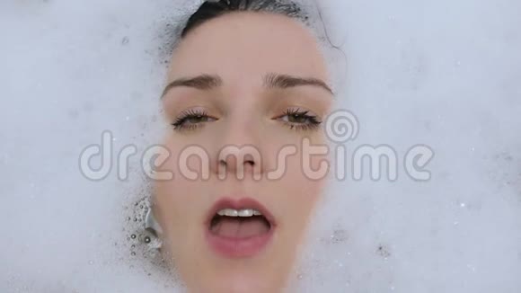 幸福的女人躺在浴室里脸上带着白色泡沫对着镜头微笑视频的预览图