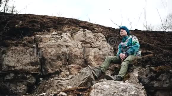 这个男孩坐在河边陡峭的斜坡上的岩石上美丽的景色视频的预览图