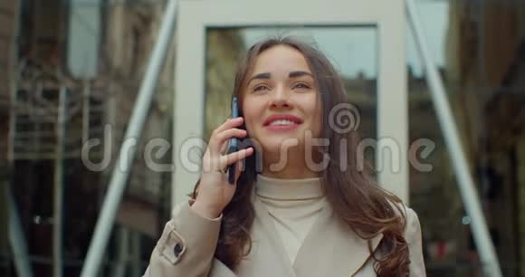 幸福的年轻女子一边走在大现代办公楼旁一边用手机说话快关门视频的预览图