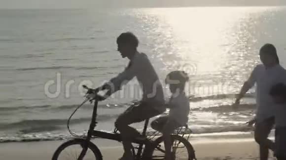 快乐的亚洲家庭父子俩骑自行车母女俩一起在海滩上散步度假视频的预览图