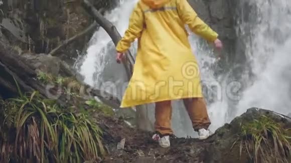 穿着黄色雨衣的年轻男性旅行者喜欢美丽的瀑布在山里远足徒步旅行者跑到视频的预览图