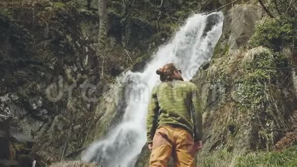 年轻的男性旅行者喜欢美丽的瀑布在山里远足徒步旅行者跑到瀑布前举起视频的预览图