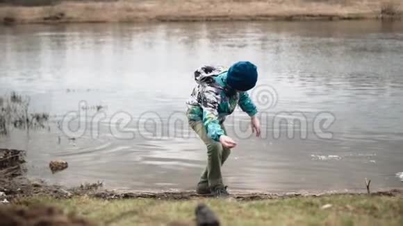 一个男孩把河岸上的石头扔进水里沿着河岸散步视频的预览图