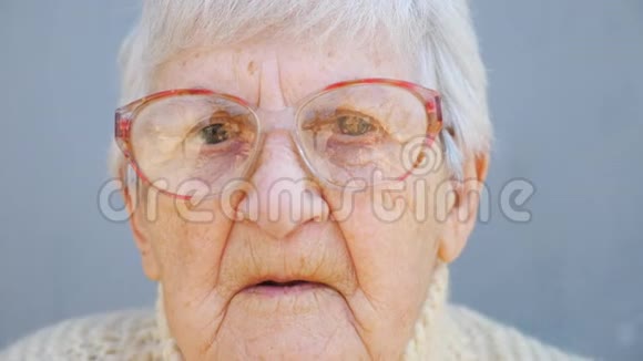 戴眼镜的老太太带着沉思的目光的肖像特写一张布满皱纹的女养老金领取者的脸看着镜头视频的预览图