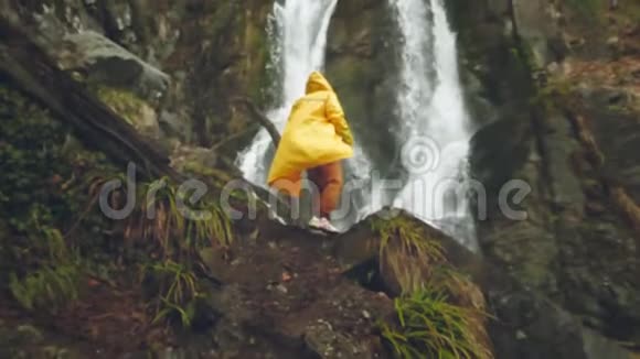 穿着黄色雨衣的年轻男性旅行者喜欢美丽的瀑布在山里远足徒步旅行者跑到视频的预览图