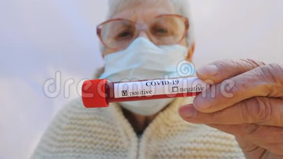 带防护面罩的老太太拿着她的血液测试冠状病毒结果阳性恶心的老奶奶视频的预览图