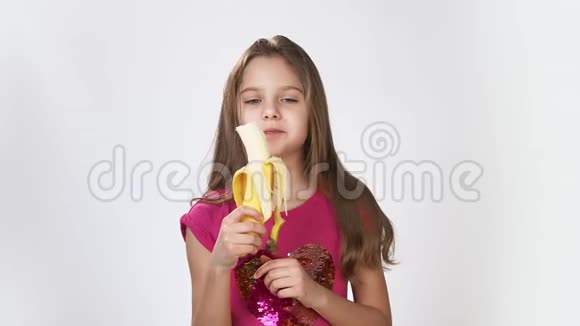 白色背景的小女孩吃香蕉一个吃香蕉的饥饿女孩的快乐情绪视频的预览图