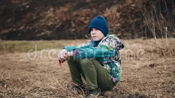 一个神情悲伤的男孩正坐在河岸上的干草上不错的镜头感情和情绪视频的预览图