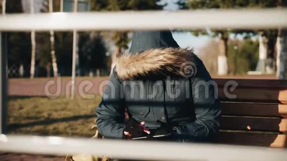 那个女孩正坐在公园里的一张长凳上看日落在引擎盖的头上视频的预览图
