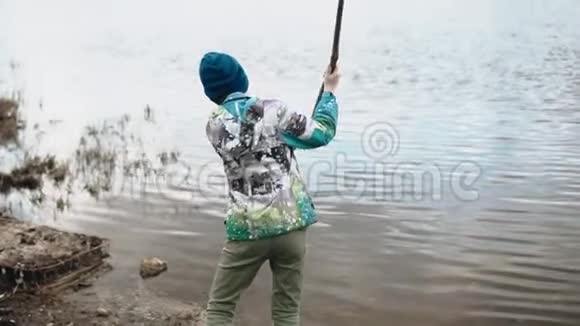 这个男孩在河岸附近的水上打了一根长树枝视频的预览图