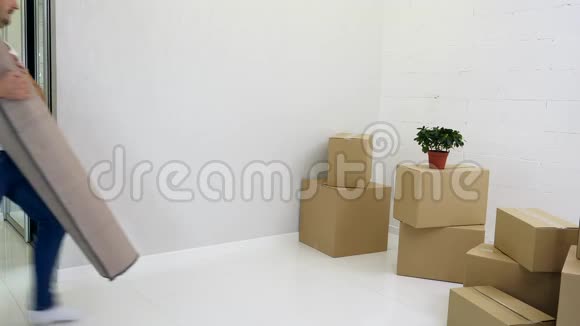 年轻夫妇在一个装满纸箱的新公寓铺上地毯视频的预览图