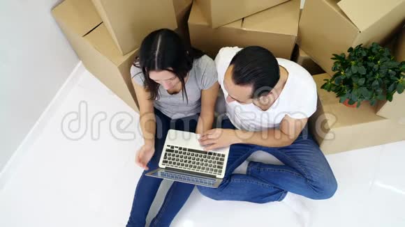 一对夫妇坐在新公寓的地板上用笔记本电脑进行网上购物选择家具和装饰视频的预览图