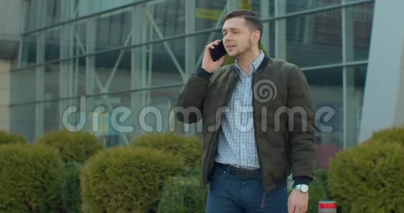 有魅力的人正兴致勃勃地在电话上讲话他走在现代办公中心附近他用的是视频的预览图