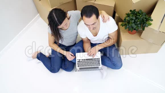 一对夫妇坐在新公寓的地板上用笔记本电脑进行网上购物选择家具和装饰视频的预览图