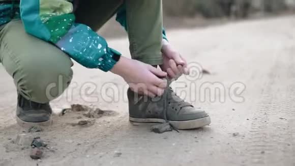 男孩把鞋带系在运动鞋上沙尘飞扬土路视频的预览图