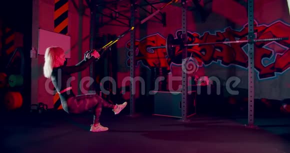 女运动员在体育馆做TRX缆绳单腿蹲侧视图视频的预览图