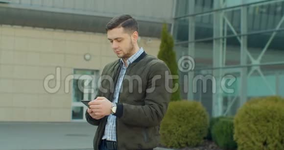 城市街道上的年轻人使用手机打字和朋友聊天男人在户外使用手机视频的预览图