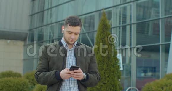 带智能手机和耳机的人在现代办公中心附近行走的肖像在社交网络上和他聊天视频的预览图