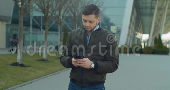 带着智能手机走在现代办公中心附近的男子肖像在社交网络上和朋友聊天看视频的预览图