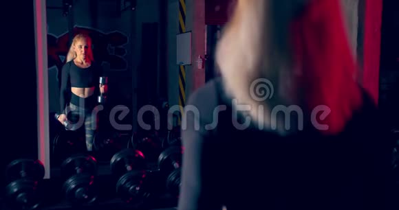 运动员女孩在镜子前举起哑铃锻炼锤在健身房辛勤工作的史诗灯视频的预览图