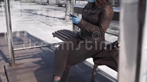 戴手术面罩和使用智能手机的女性坐在公共汽车站视频的预览图