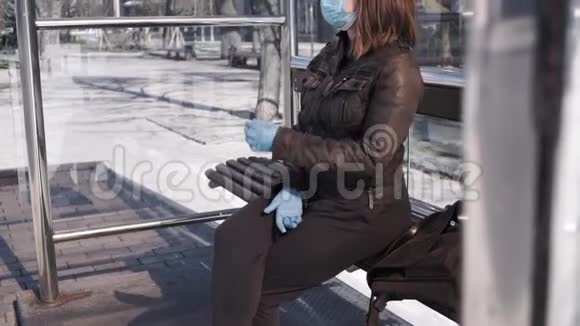 戴着外科口罩和乳胶手套的女性坐在公共汽车站视频的预览图