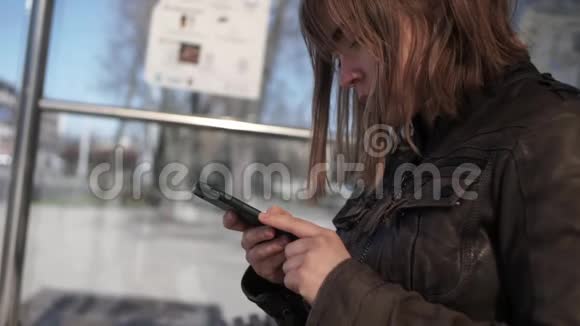 坐在公交车站的YounWomen使用智能手机视频的预览图