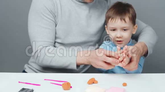 父亲和儿子在灰色背景下雕刻塑料玩具的视频视频的预览图