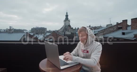 一个年轻人坐在屋顶上拿着笔记本电脑背景是一个古老的城市景色视频的预览图