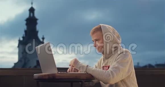 一个年轻人坐在屋顶上拿着笔记本电脑背景是一座古老的城市塔楼视频的预览图