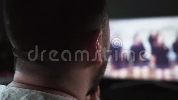 一个长胡子的白人男子在家里看电视屏幕上的狱卒录像视频的预览图