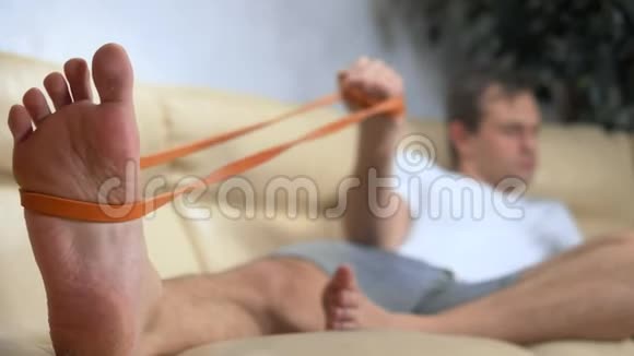 沙发上的男人用弹力带做运动用智能手机视频的预览图