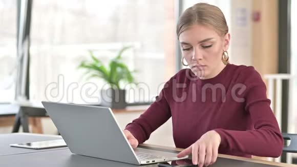 办公室智能手机上有笔记本电脑的年轻女子视频的预览图