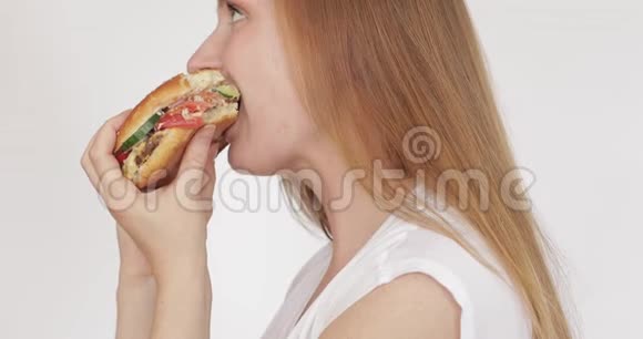 可爱的饥饿的女人吃了一个大汉堡在白色背景下微笑着视频的预览图