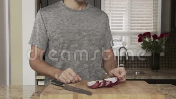 年轻的帅哥在一把大菜刀旁边的木板上的桌子上清理厨房里的红洋葱视频的预览图
