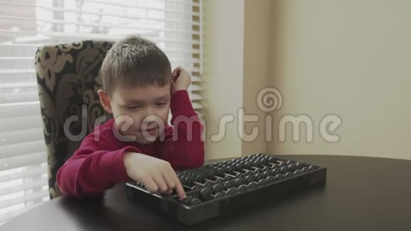 穿着红色毛衣的小学生坐在桌子旁用旧算盘学习数学快乐的孩子教算盘数学视频的预览图