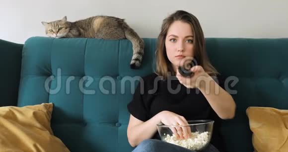 女人吃爆米花坐在沙发上在家里切换频道遥控器视频的预览图