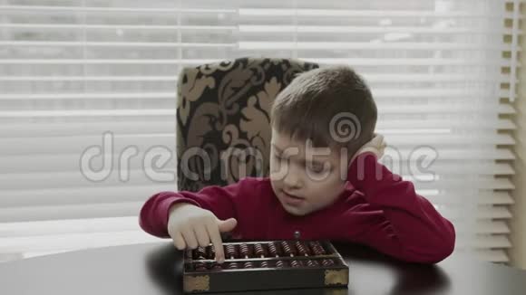 穿着红色毛衣的小学生坐在桌子旁用旧算盘学习数学快乐的孩子教算盘数学视频的预览图