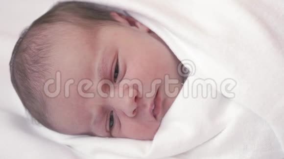一个新生婴儿穿着白色尿布微笑的特写镜头白色背景下的特写宝宝醒来微笑做鬼脸视频的预览图