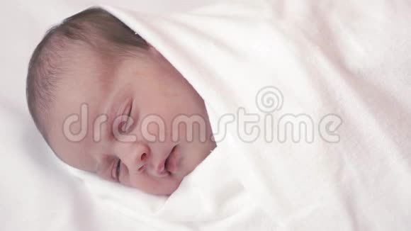 一个新生婴儿穿着白色尿布微笑的特写镜头白色背景下的特写宝宝醒来微笑做鬼脸视频的预览图