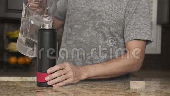 穿着灰色T恤的年轻人在一个漂亮时尚的厨房里用塑料瓶把水倒进热水瓶视频的预览图