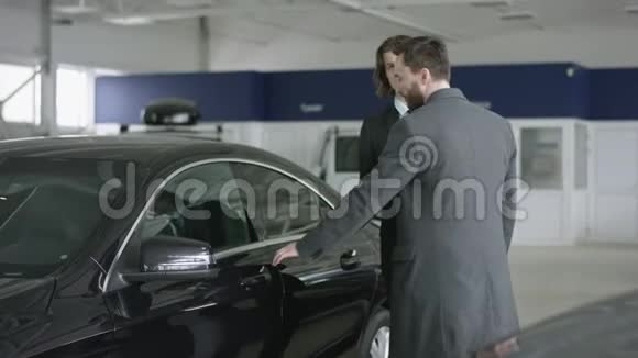 汽车经销商客户坐在车里汽车经销商为汽车买家打开了一扇门愉快的客户与交易员交谈视频的预览图