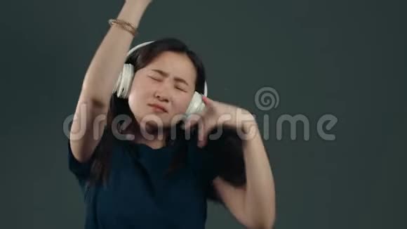 年轻漂亮的亚洲女孩留着长发玩得开心微笑着戴着耳机在灰色背景的工作室里跳舞视频的预览图