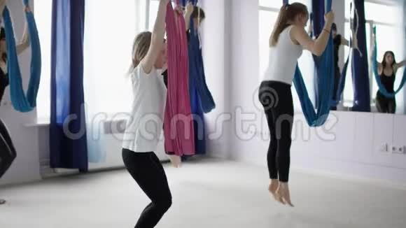 年轻的运动女性跳入空中瑜伽吊床并在反重力瑜伽工作室中保持平衡视频的预览图