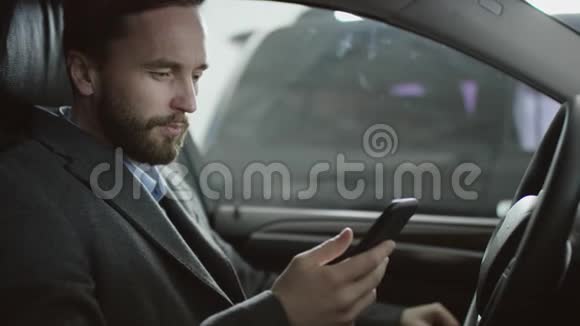 一个商人坐在驾驶座上的汽车上用他手机上网接待商人视频的预览图