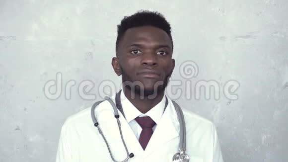 一位非洲男医生站在白色实验室外套上靠在混凝土墙上的肖像从他的听诊器上取出一个听诊器视频的预览图